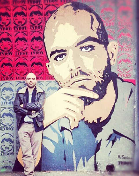 Roberto Saviano in posa accanto al murale realizzato da TvBoy (480x608cm)